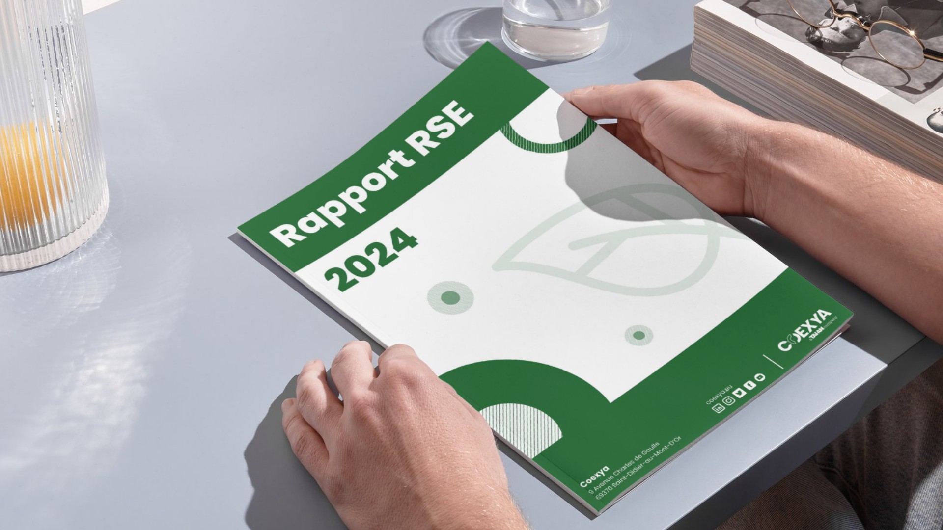 Mains tenant la couverture verte et blanche du Rapport RSE 2024 du groupe Coexya, invitant au téléchargement de l'édition augmentée sur les engagements éthiques et sociétaux.